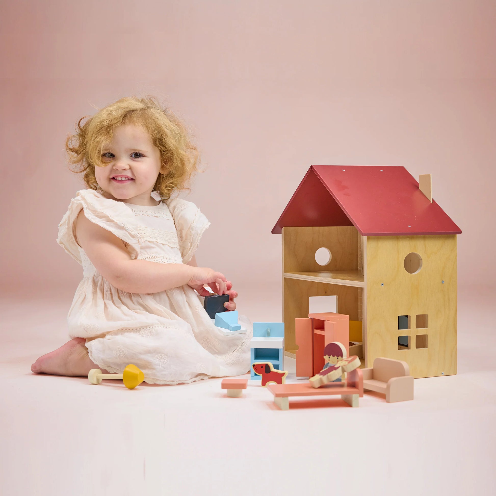 Child playing with wooden toys including a dollhouse on a pink background