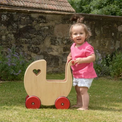 Child pushing a wooden doll pram outdoors near a stone wall.
