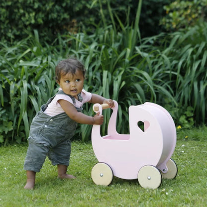 Child playing with a pink toy pram in a garden setting