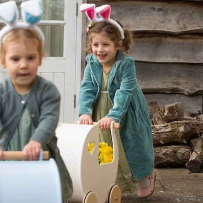Two children playing with a toy cart outdoors, one wearing bunny ears.