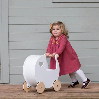 Child in a pink dress pushing a white toy pram on a wooden deck.