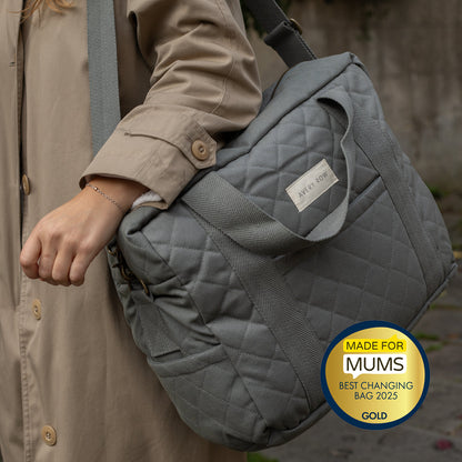 Gray quilted changing bag held by a person, with a 'Made for Mums' award badge.