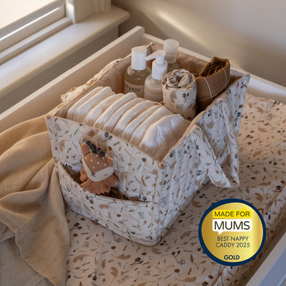 Fabric nappy caddy with baby items on a changing table, featuring a 'Made for Mums' award badge.