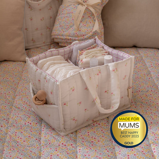 Nappy caddy with baby items on a floral blanket, featuring a 'Made for Mums' award badge.