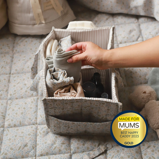 Hand reaching into a fabric nappy caddy on a quilted surface with a 'Made for Mums' award badge.