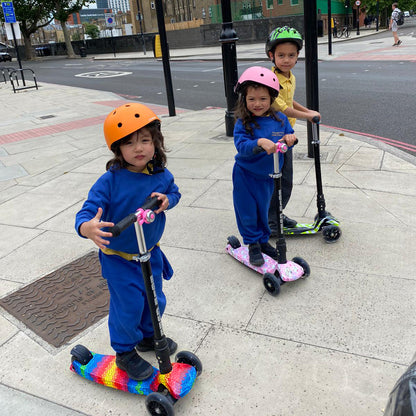 Children riding scooters on a sidewalk with helmets