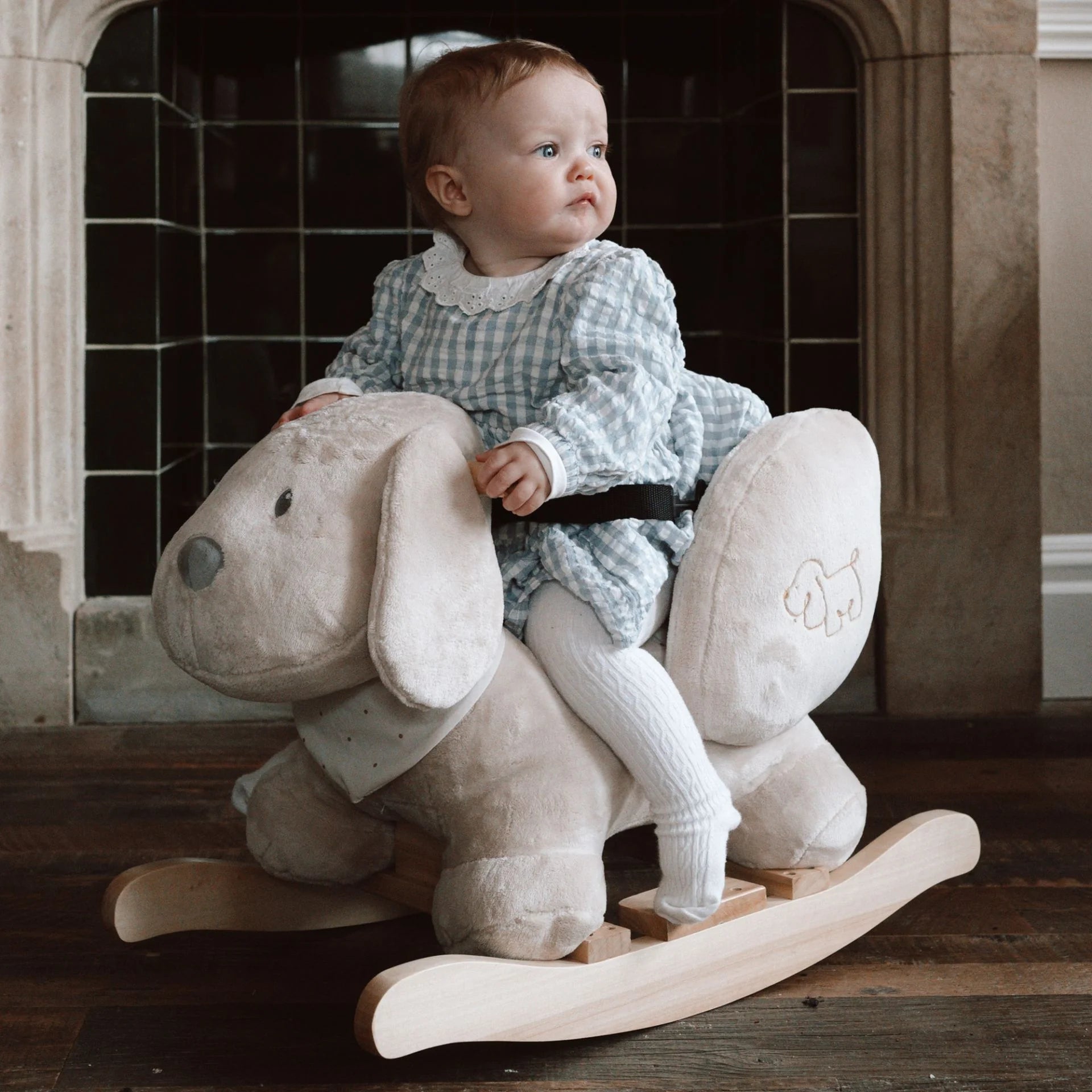 Baby sitting on a rocking horse in a room with tiled walls.