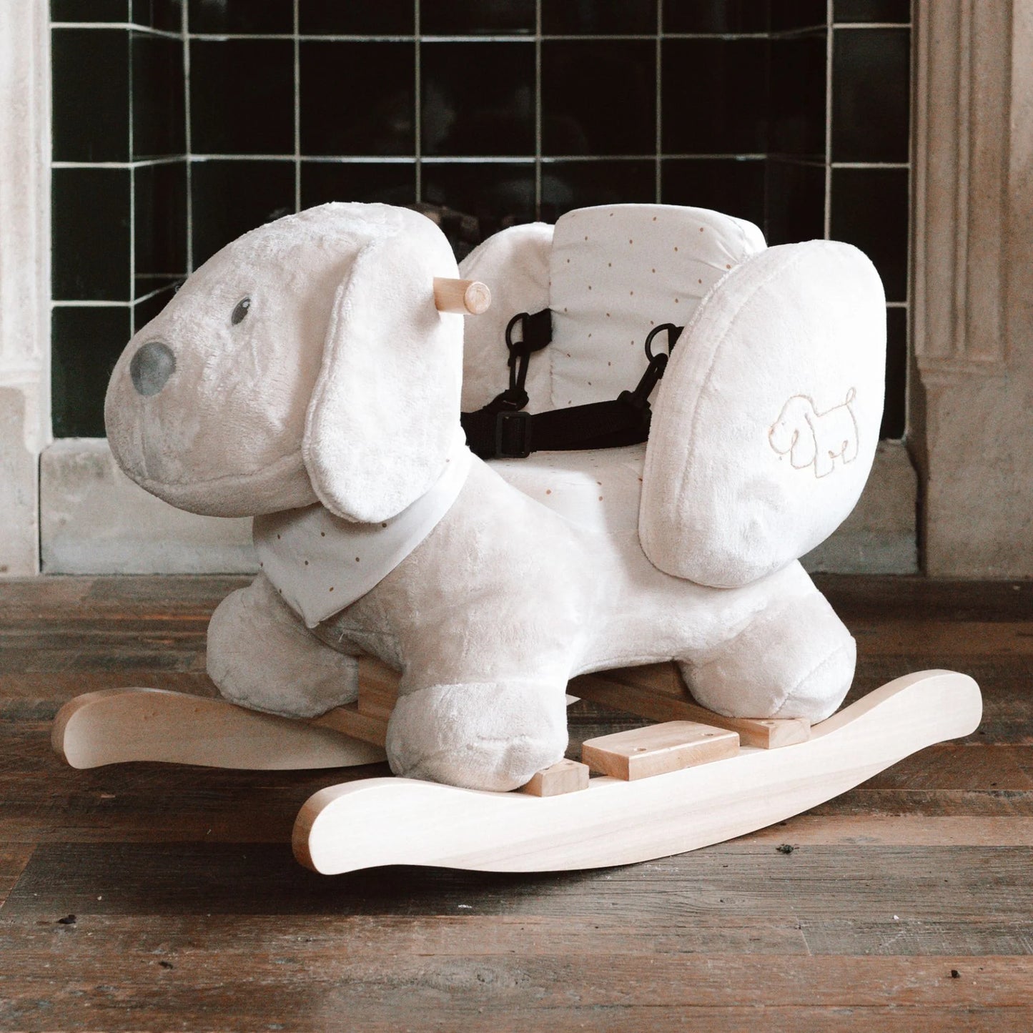 Plush dog-shaped rocking toy on a wooden floor with a tiled wall in the background