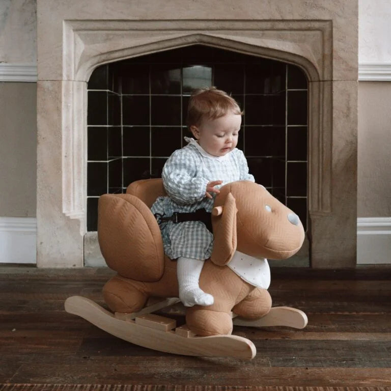 Child sitting on a rocking horse in front of a fireplace