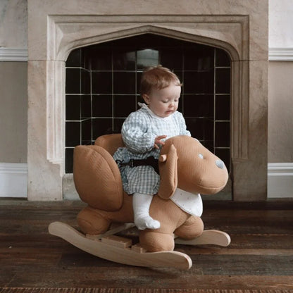 Child sitting on a rocking horse in front of a fireplace