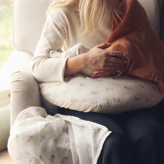 Person sitting on a couch holding a baby wrapped in a blanket with a floral pattern.