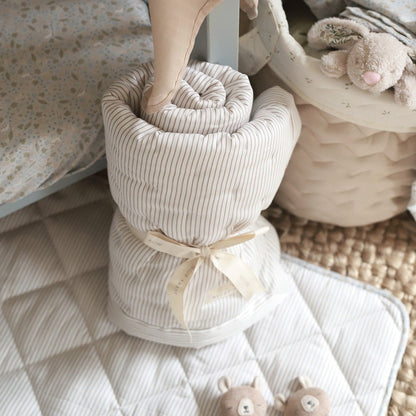 Folded striped towel with a ribbon, placed on a textured surface with soft toys in the background.