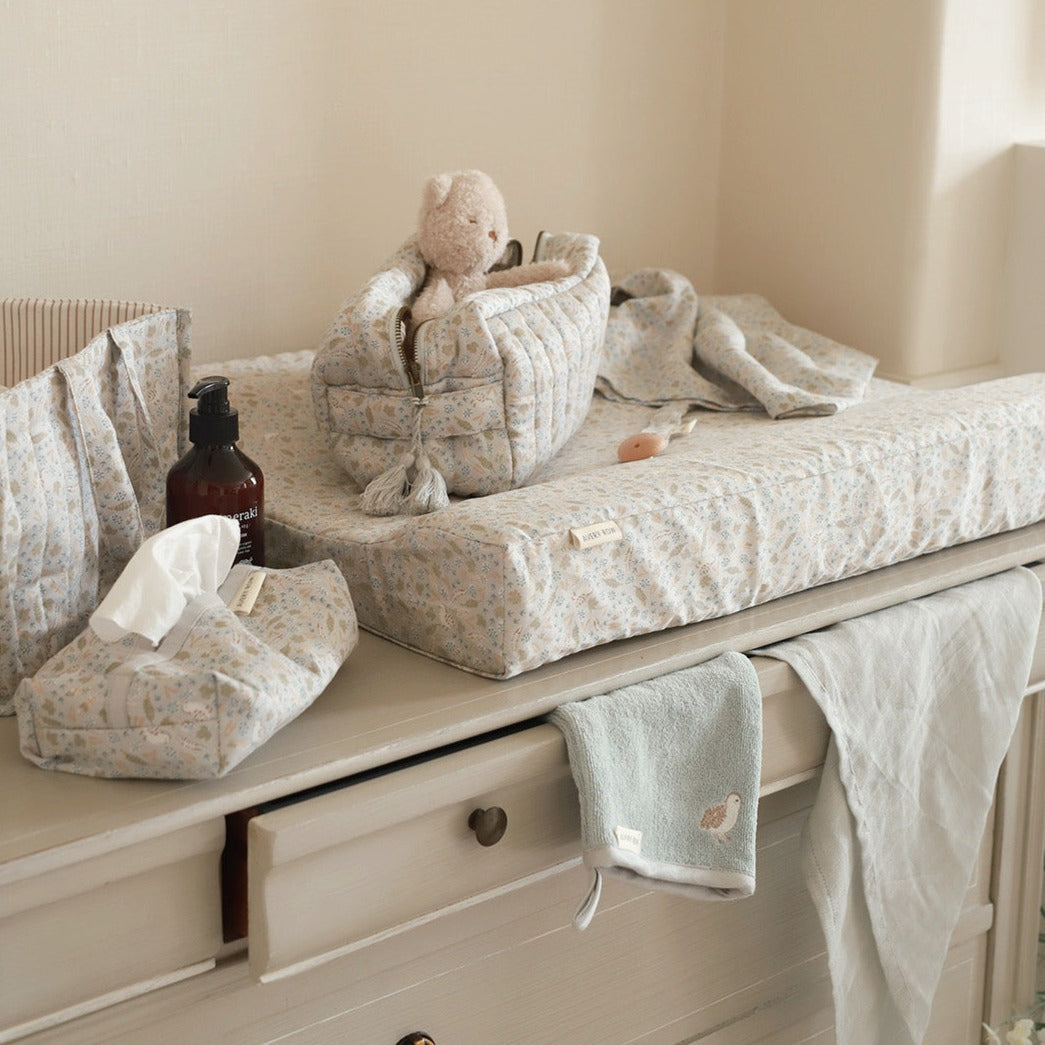 Baby changing table with baby items including a teddy bear, tissues, and a bottle.