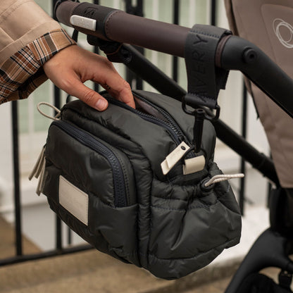 Black pouch attached to a stroller with a hand reaching towards it.