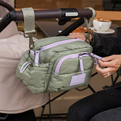 Green waist bag with purple zippers attached to a stroller handle.