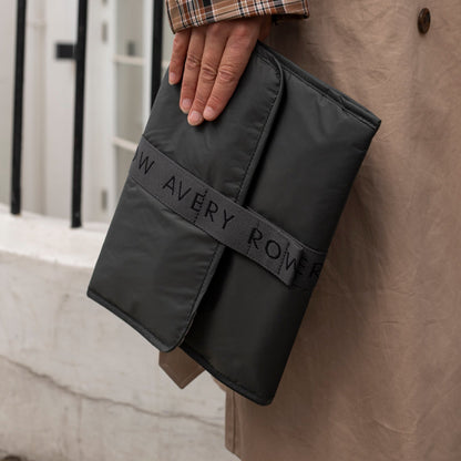 Black fabric roll with 'W Avery Rover' branding held by a person against a beige wall.
