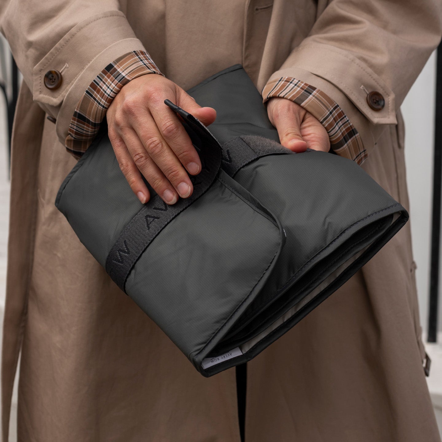 Person holding a black wallet with 'WANDL' branding, wearing a beige trench coat.