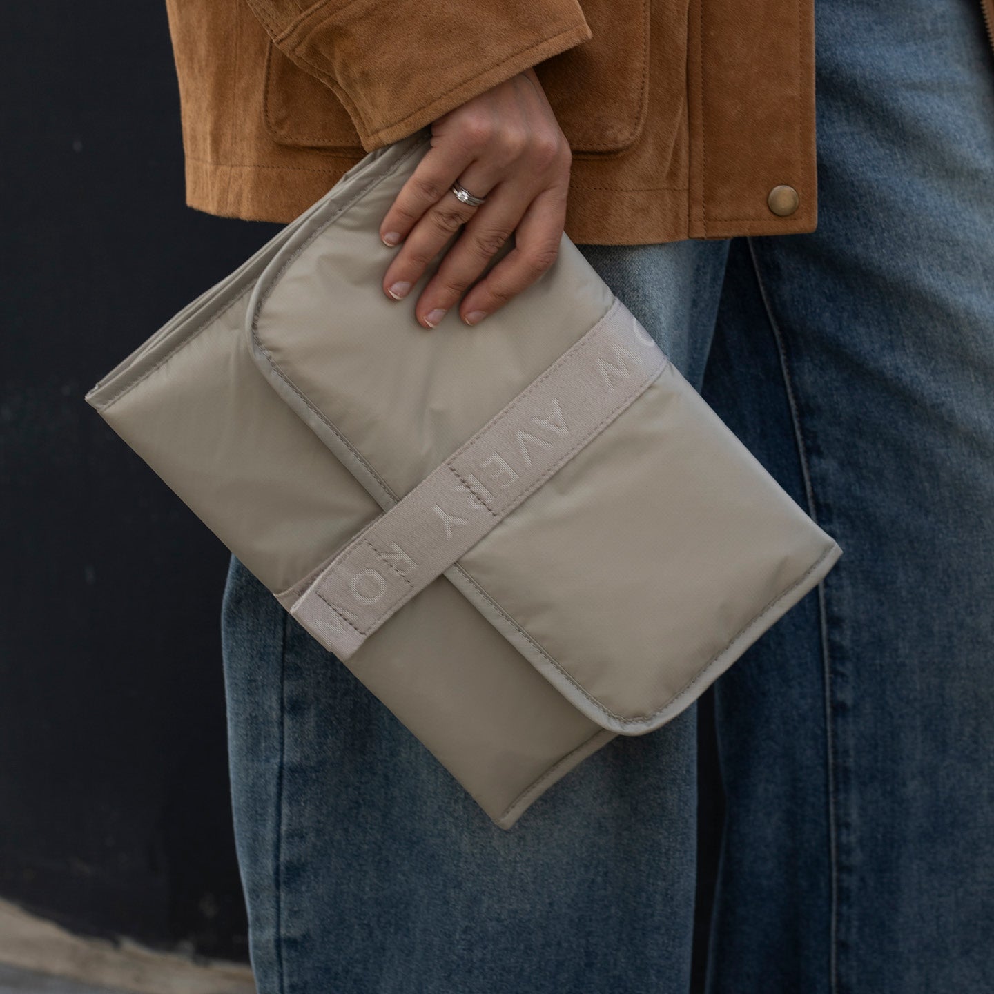 Person holding a beige clutch bag with 'Kow Kow' branding.