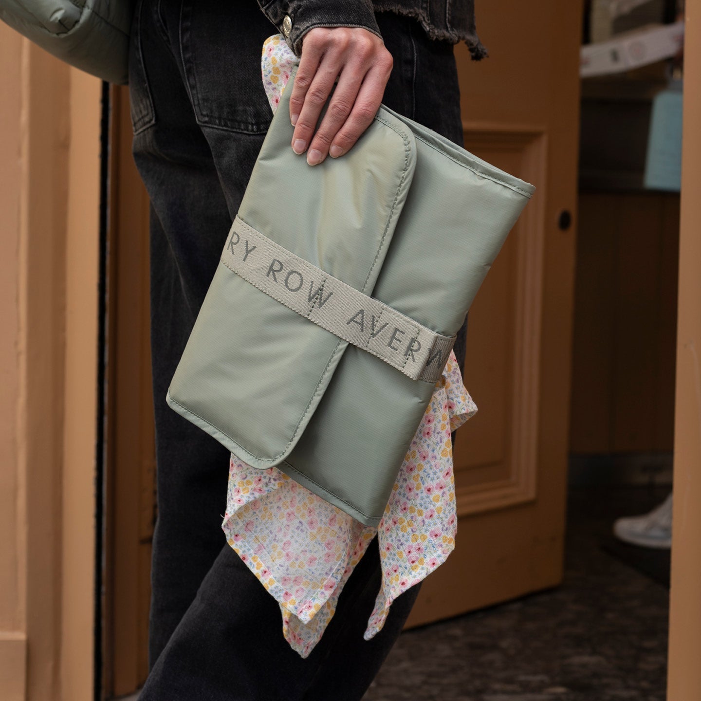Person holding a green fabric item with 'Row Aver' branding against a wooden door background.