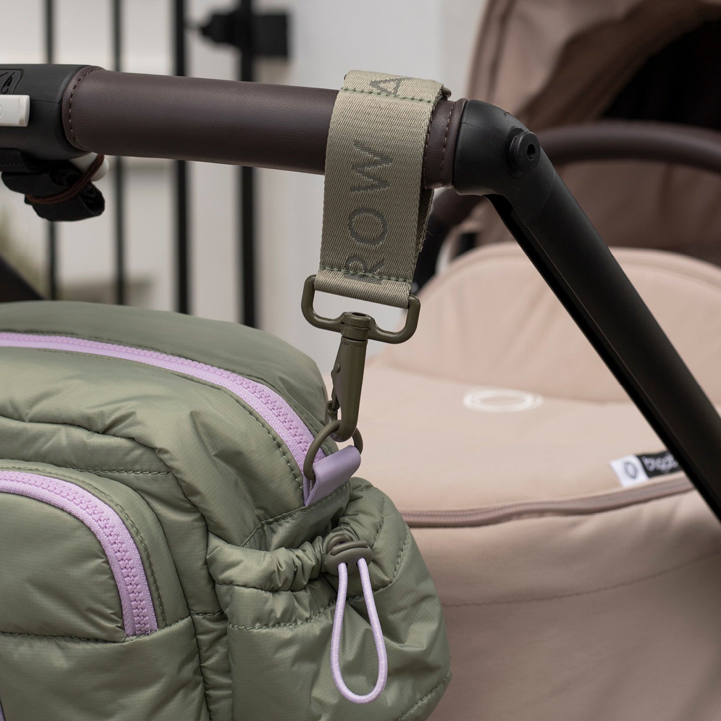 Close-up of a stroller handle with a green jacket draped over it, featuring the brand 'Rowa'.