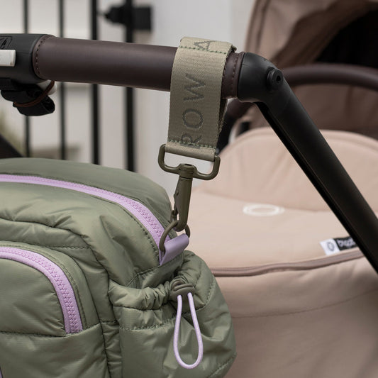 Close-up of a stroller handle with a green jacket draped over it, featuring the brand 'Rowa'.