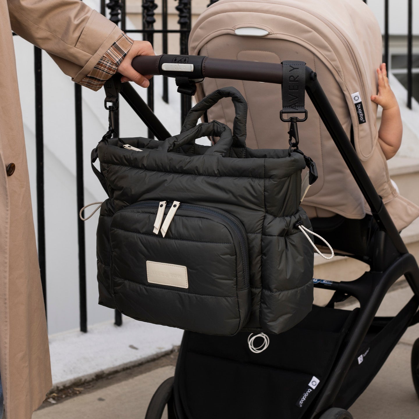 Black stroller bag attached to a beige stroller with a person holding it.
