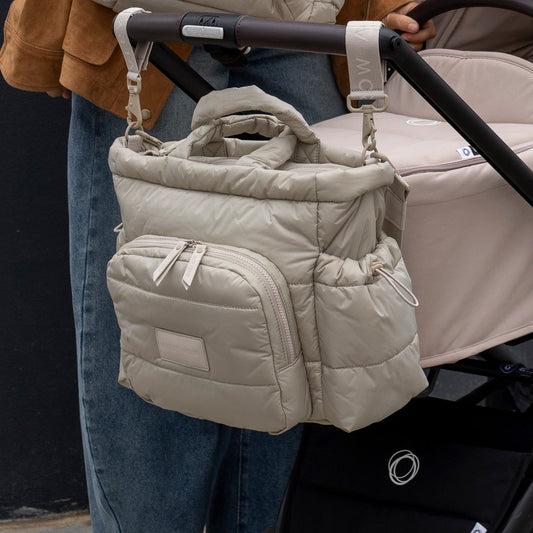 Beige puffer bag attached to a stroller with a person holding it.
