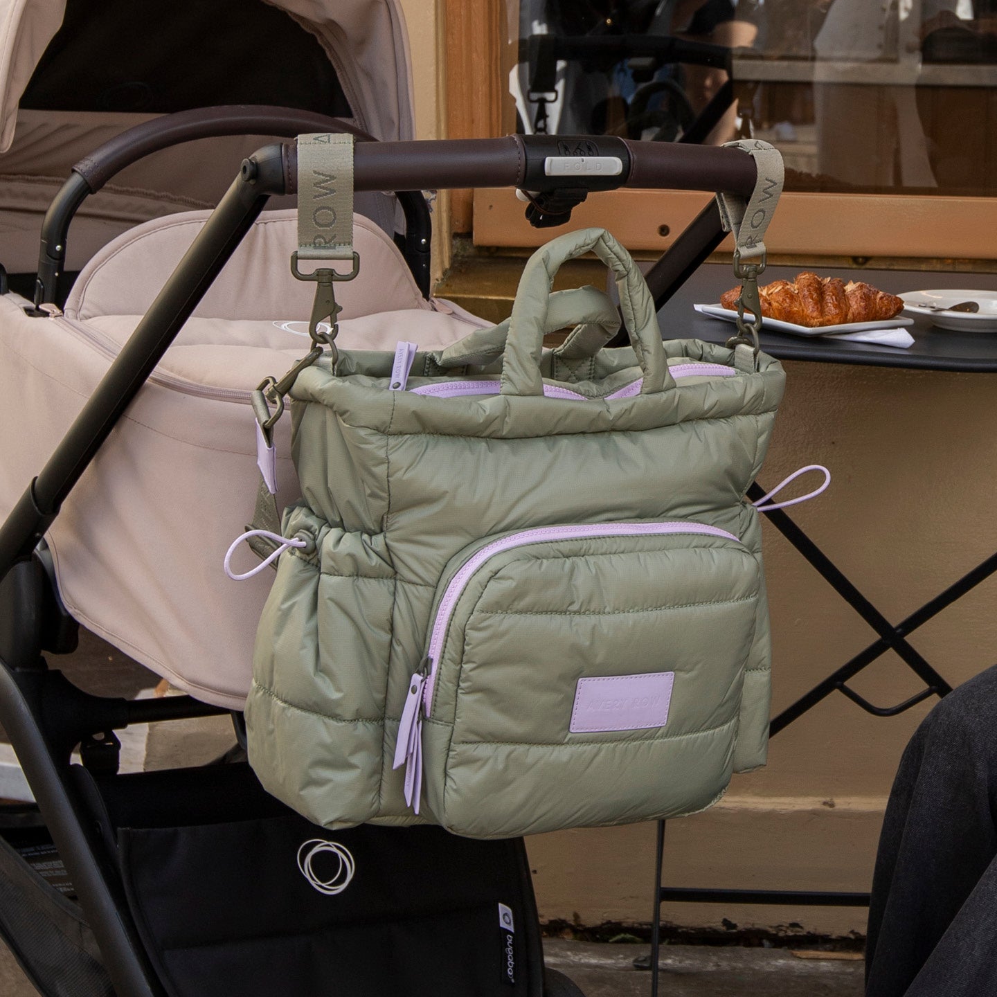 Green puffer bag hanging from a stroller handle with a blurred background