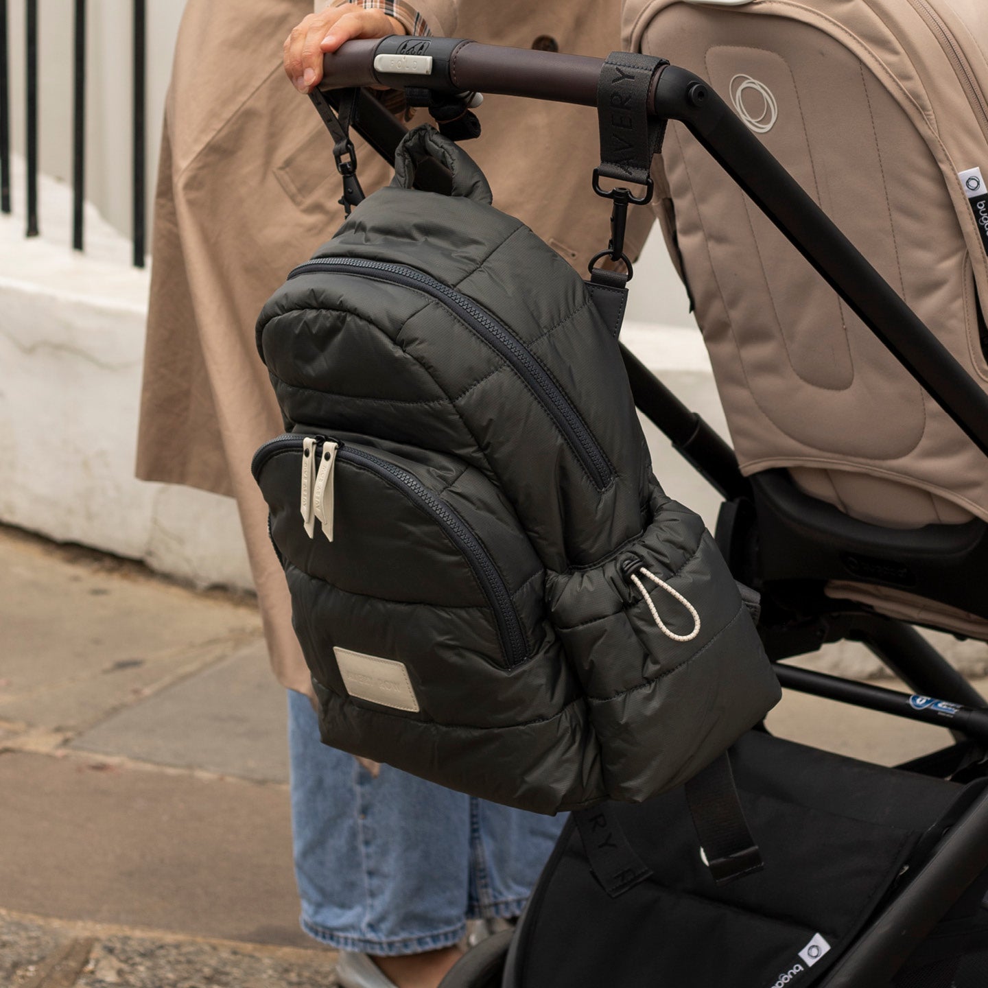 Person holding a black insulated bag attached to a stroller on a sidewalk.