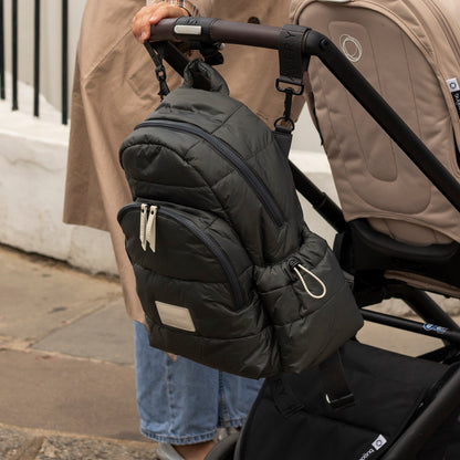 Person holding a black insulated bag attached to a stroller on a sidewalk.