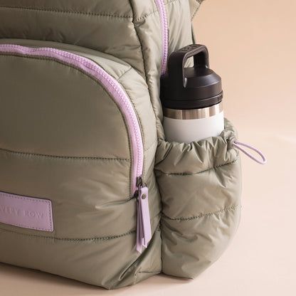 Green backpack with pink zipper and water bottle on a beige background