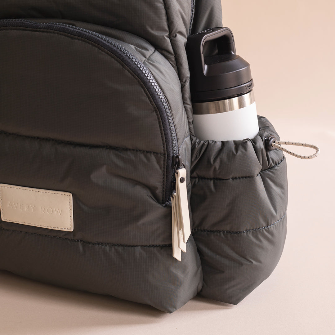 Black backpack with a water bottle attached on a beige background
