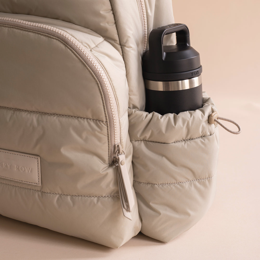 Beige backpack with a water bottle in a pocket on a beige background