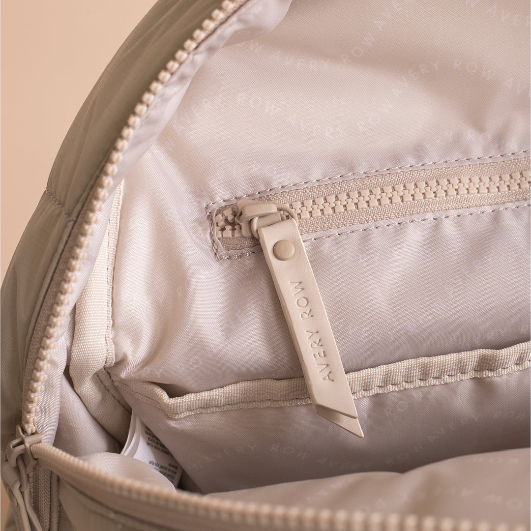 Close-up of a beige backpack with a visible brand tag on a beige background