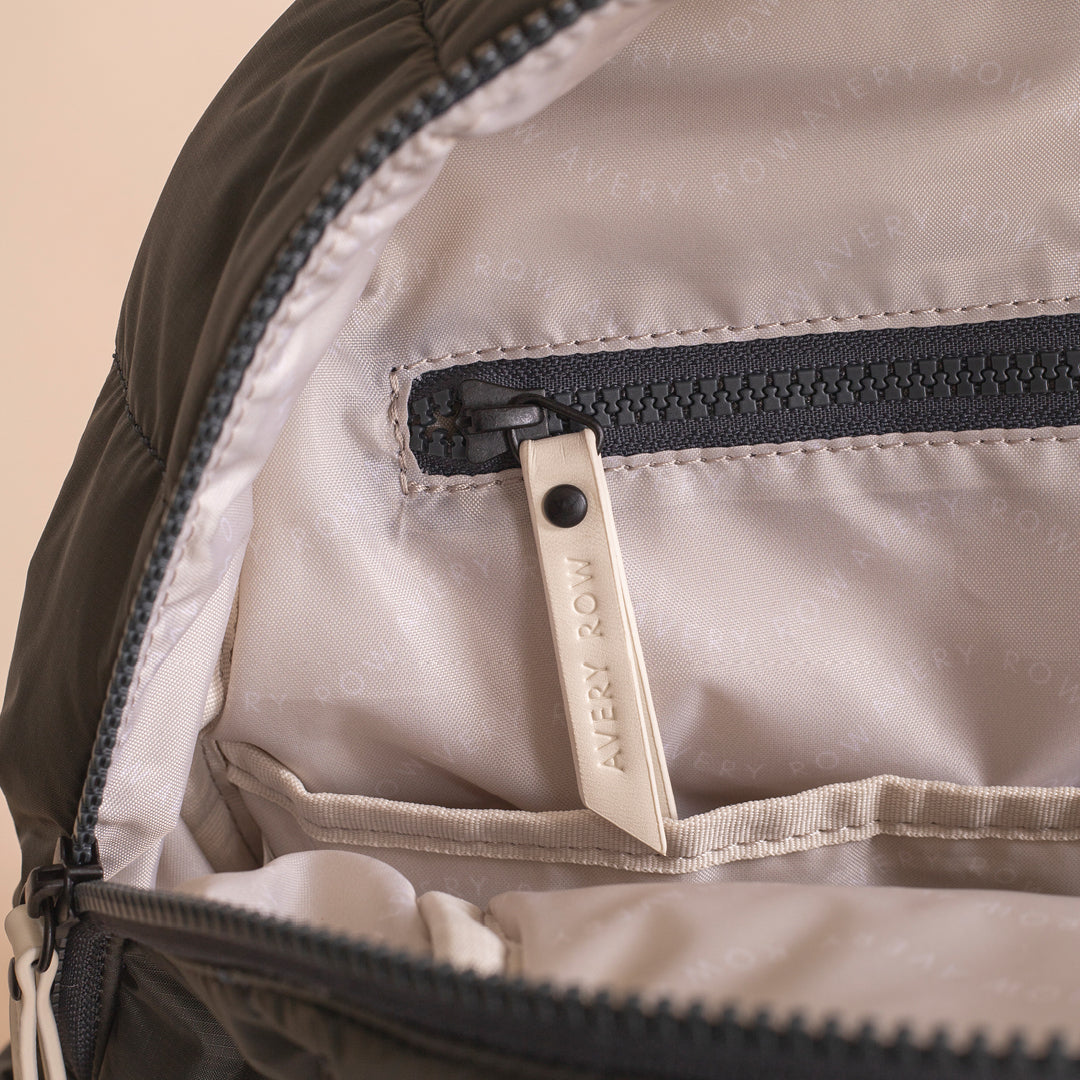 Close-up of a backpack zipper with 'Every Row' brand tag on beige fabric.