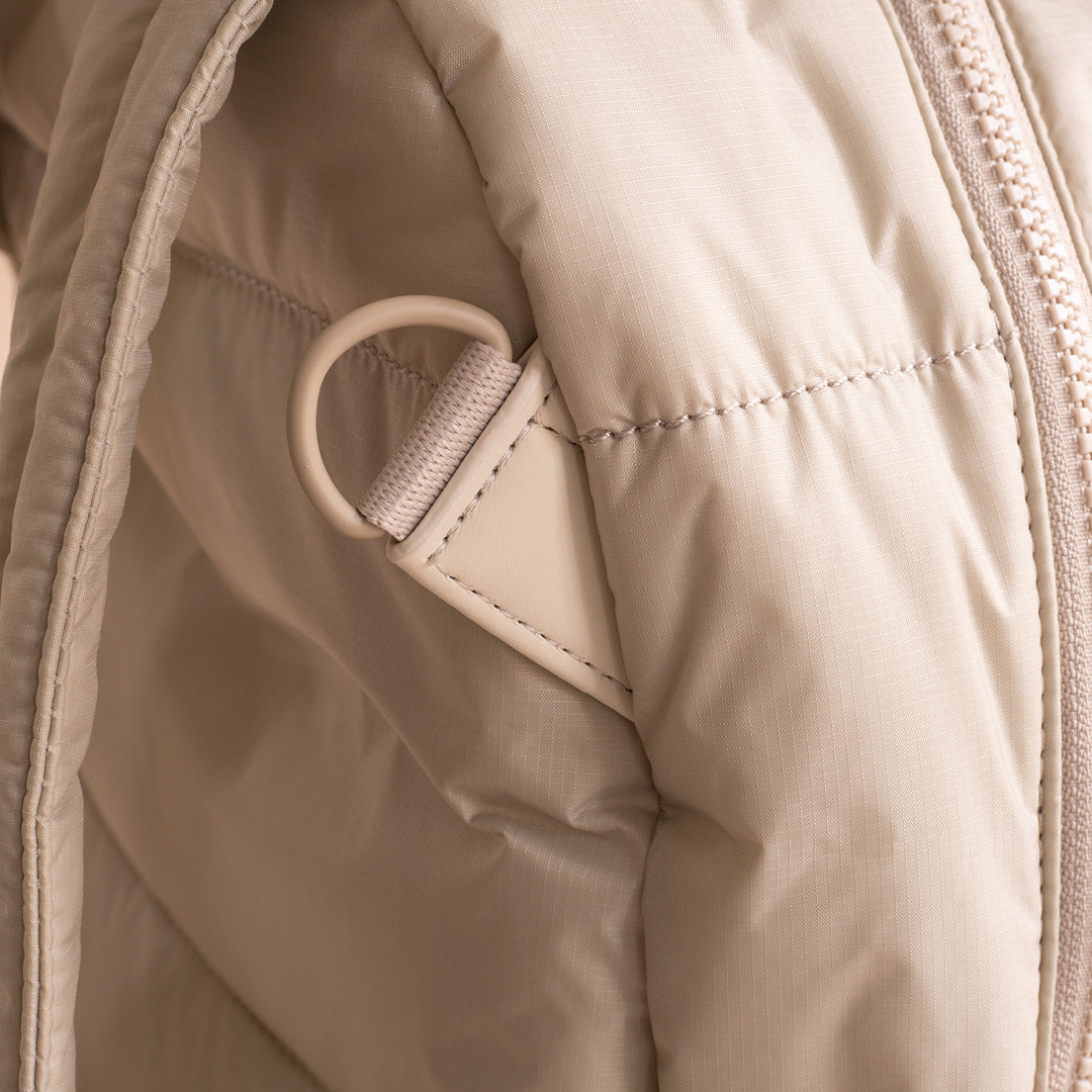 Close-up of a beige quilted jacket with a zipper and button detail.