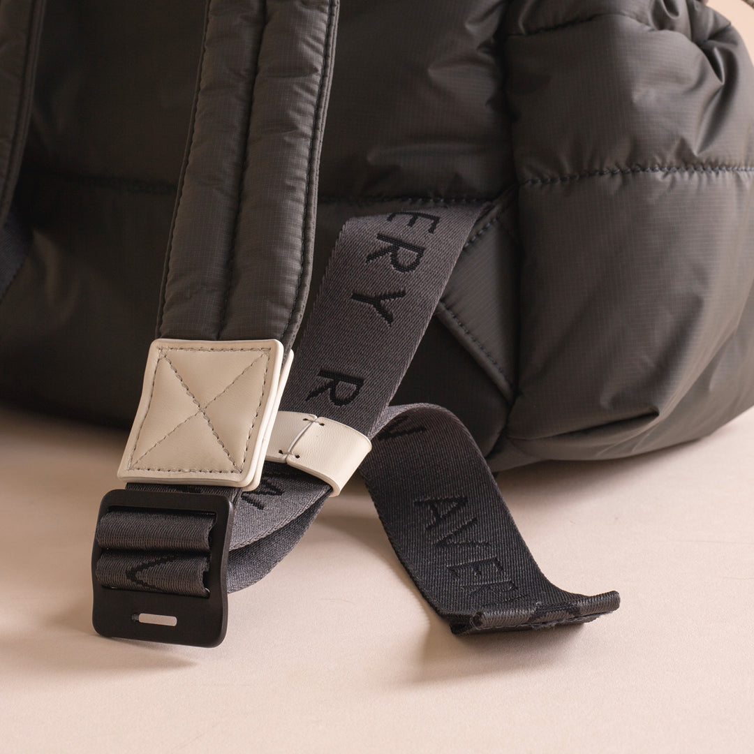 Close-up of a black puffer jacket with a visible brand label on a beige background