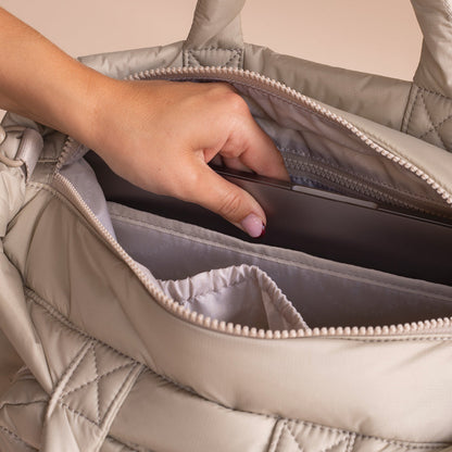 Hand reaching into a quilted beige bag to retrieve a phone.