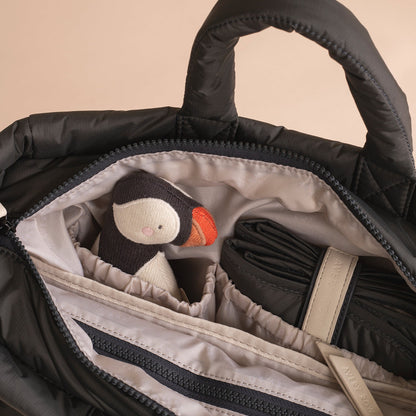Black bag with a penguin plush toy inside, beige background
