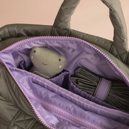 Gray plush toy inside a green quilted bag with purple lining