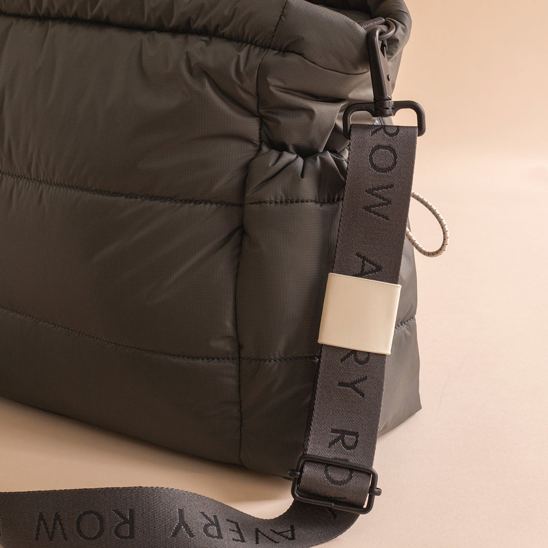 Close-up of a dark gray backpack with a visible brand strap on a beige background
