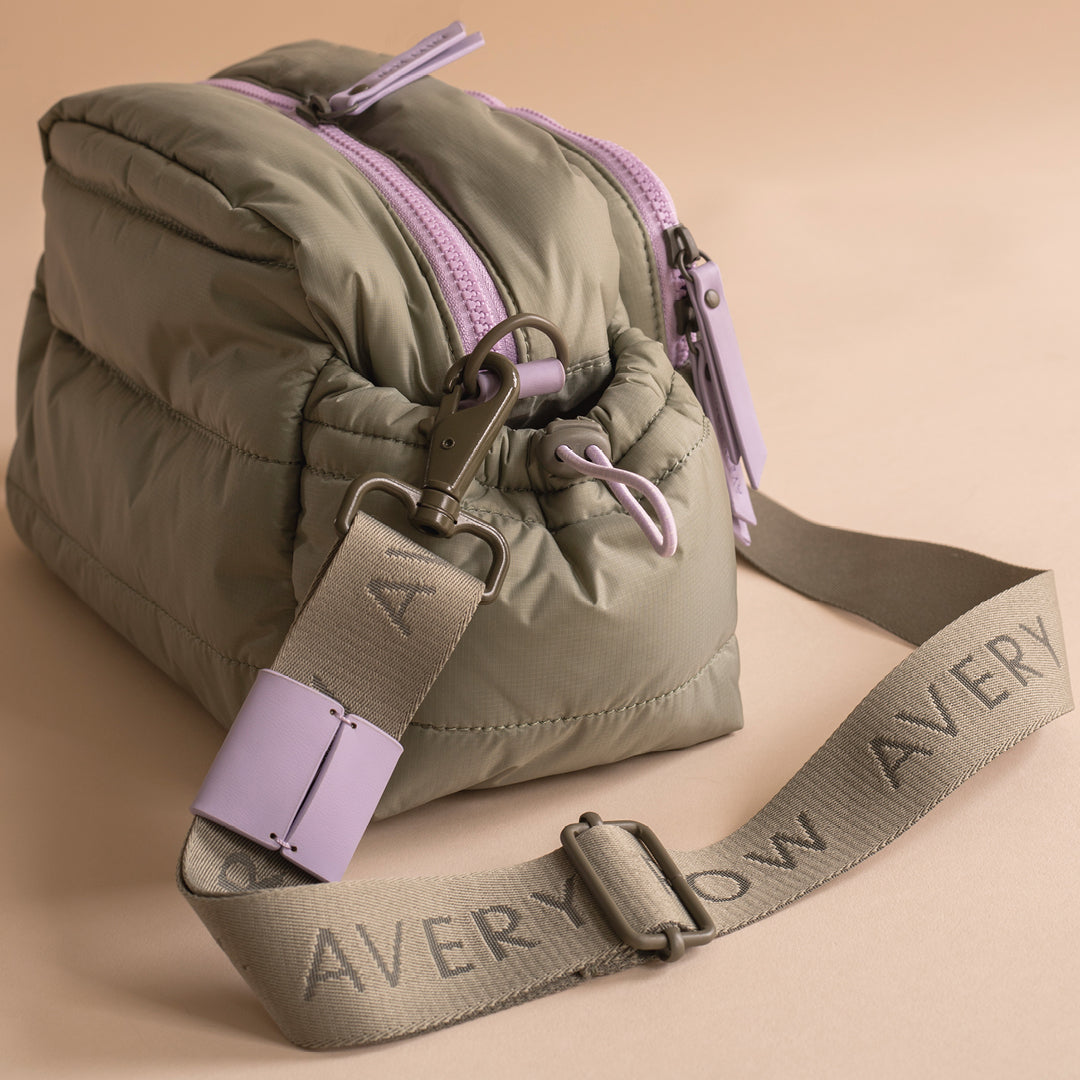 Green puffer bag with purple zippers and strap on a beige background
