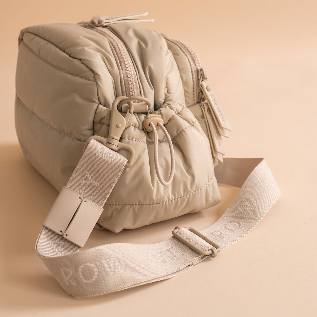 Beige puffer bag with matching strap on a beige background