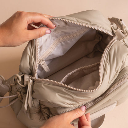 Beige backpack with a hand opening it on a beige background