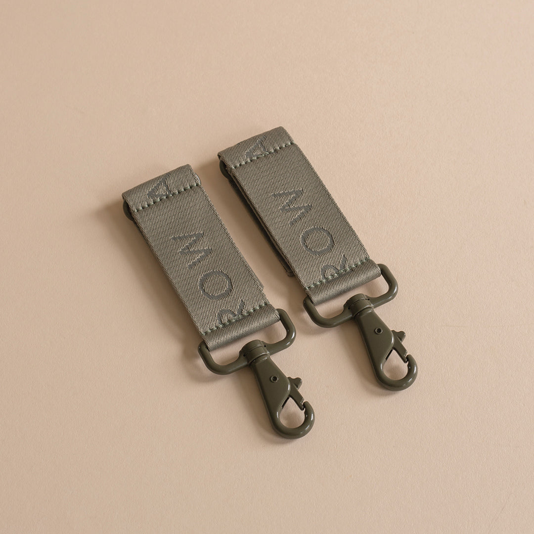 Two green leather straps with metal hooks on a beige background