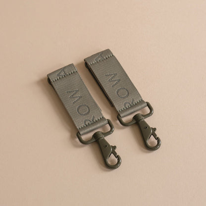 Two green leather straps with metal hooks on a beige background