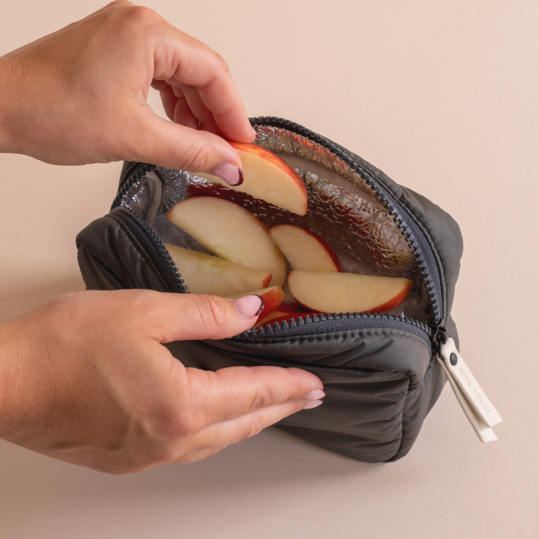Person holding a small insulated bag with sliced apples inside, on a beige background