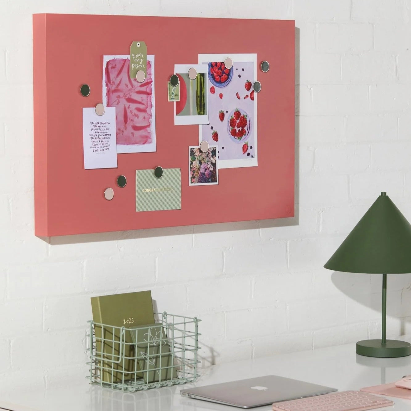 Pink cork bulletin board with pinned items on a white wall above a desk.