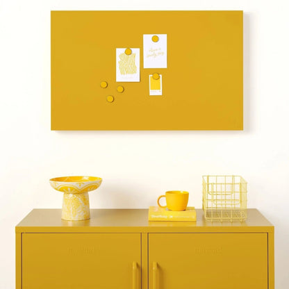 Yellow cabinet with a matching yellow bulletin board above it on a white wall.