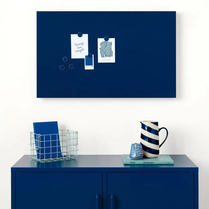 Navy blue magnetic board on a white wall above a blue cabinet with decorative items.